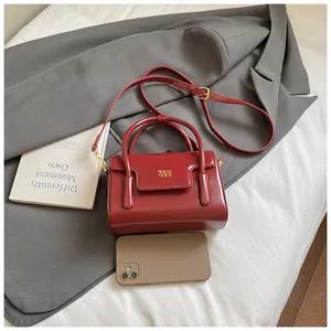 Close-up of burgundy leather mini box bag with gold logo and phone for size scale
