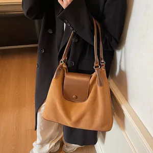 Detail view of large brown suede shoulder bag featuring a round clasp on front flap
