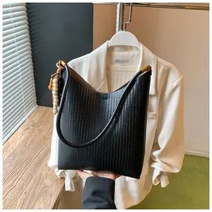Détail du sac sous l'aisselle tressé noir avec gland en perles de bois et bijoux dorés