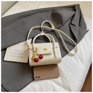 Detail of cream square handbag with gold logo, cherry pendant and crossbody strap