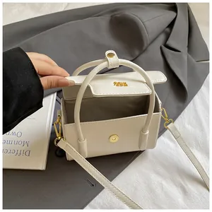 Detail of white leather-like crossbody bag with golden logo and magnetic closure