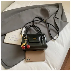 Mini black glossy crossbody bag with cherry pendant and adjustable shoulder strap