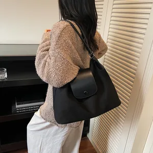Detail of black matte leather tote bag featuring a round snap button and slim strap