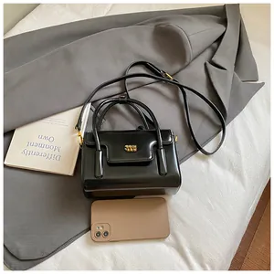 Detail view of a black glossy handbag with gold logo, shoulder strap and casual props