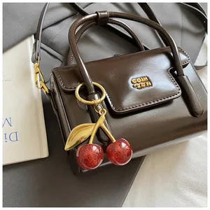Detail of dark brown glossy handbag with golden logo and cherry charm accessory
