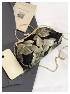 Détail d'un sac à main brodé de fleurs vintage avec poignée en métal doré et chaîne