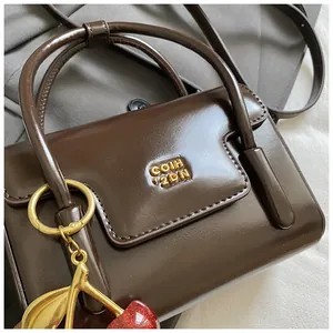 Detail of dark brown glossy leather handbag with gold logo and cherry pendant accessory