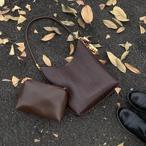 Vue à plat d'un sac à bandoulière marron foncé tissé avec une pochette sur fond d'asphalte