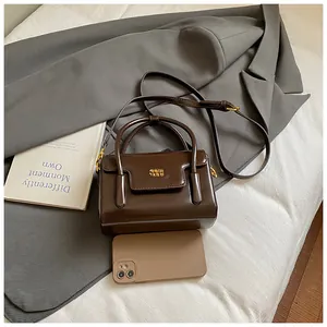 Detail of dark brown glossy handbag with gold metal logo and phone for size reference