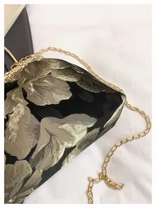 Détail de la broderie florale dorée et du fermoir serti de diamants sur le sac de soirée noir