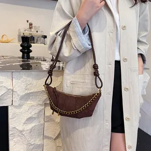 Bolso de media luna marrón mate con cadena dorada usado sobre una gabardina beige