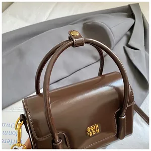 Close-up of deep brown glossy leather handbag with gold metal hardware and circular handles