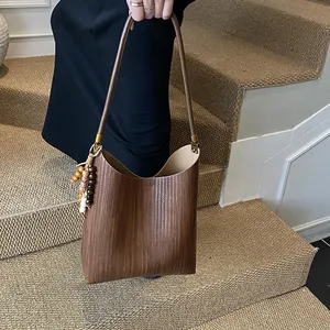 Sac fourre-tout en cuir tissé marron avec charme en perles de bois tenu par un modèle