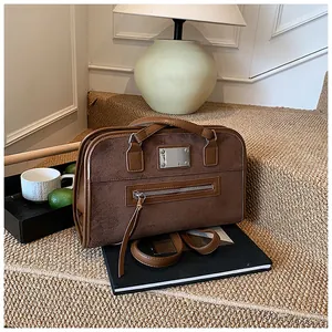 Détail du sac Boston marron avec deux poignées et plaque en métal sur un tapis texturé