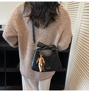 Detail of black dumpling bag featuring bow handle and colorful bead tassel accessory