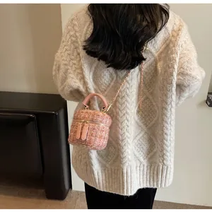 Rosa Tweed-Beuteltasche mit goldener Kette über einem weißen Strickpullover