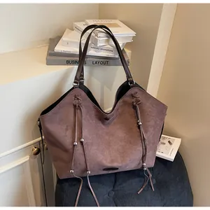 Detail view of large faux suede tote bag with fringe and metal beads in a cozy studio setting