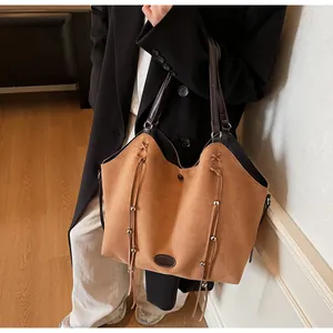 Brown suede tote bag with fringe tassels and metal beads worn by a model in a blazer