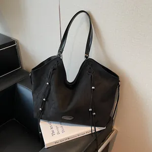 Minimalist black suede tote bag with fringe details and silver beads on a leather sofa