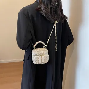 Sac bandoulière en tweed beige avec chaîne dorée porté sur un manteau noir vue de dos