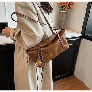 Detail of a shiny brown leather shoulder bag with a baseball glove charm on a trench coat