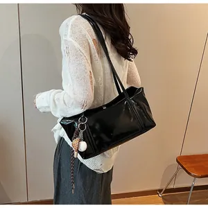Detail of glossy black patent leather shoulder bag with unique baseball themed pendant