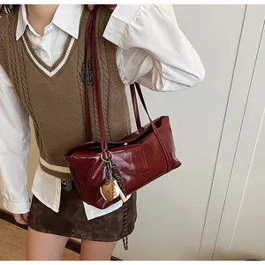 Detail of dark red patent leather shoulder bag with baseball charm and crinkled texture