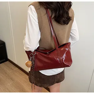 Detail of burgundy patent leather tote with brand logo and baseball charm accessory