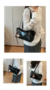 Detail of a black glossy shoulder bag featuring a sleek finish and a cute baseball charm
