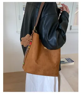 Brown suede bucket bag with shoulder strap featuring a cute teddy bear charm and colorful beads