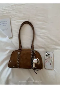 Détail du sac bandoulière vintage en daim marron avec œillets et breloques de baseball