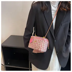 Dettaglio borsa a tracolla in tweed rosa con catena dorata indossata su un blazer nero