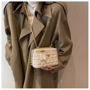 Détail du mini sac seau en tweed crème avec emblème fleur dorée et bandoulière chaîne