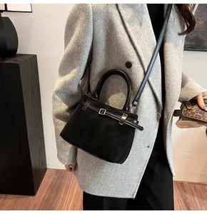 Detail of matte black bucket bag with buckle strap on a model wearing a grey suit