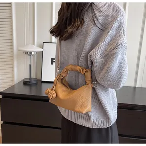 Detail of a brown leather shoulder bag featuring a unique twisted handle and side charms