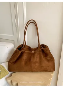 Close-up of caramel brown suede tote bag featuring slim straps and gold circular buckle