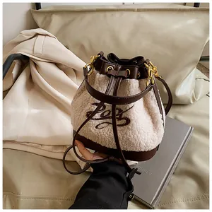 Close-up of cream faux shearling bucket bag with brown leather trim and gold hardware