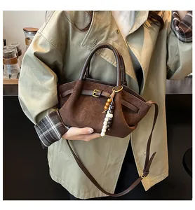 Detail of dark brown suede handbag featuring wooden bead charm and long shoulder strap
