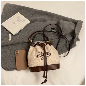 Top-down detail of fuzzy shearling bucket bag with leather trim on wool coat background