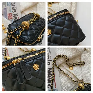 Détail du sac boîte noir matelassé avec bandoulière chaîne dorée et breloque camélia