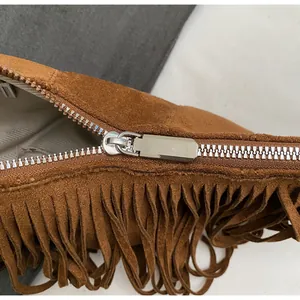 Close-up of brown suede bag featuring silver metal zipper and long fringe decorative details
