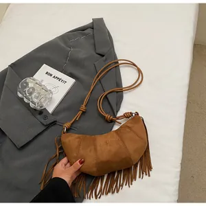 Macro detail of brown suede crescent bag featuring long tassels and knotted strap design