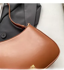 Detail of a brown leather crescent shoulder bag with elegant gold metal logo lettering