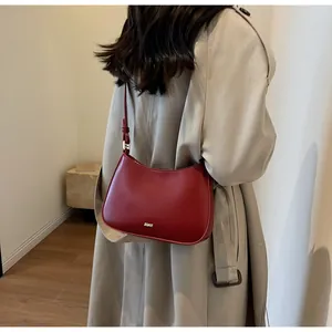 Detail view of the deep red crescent underarm bag with gold logo on a trench coat