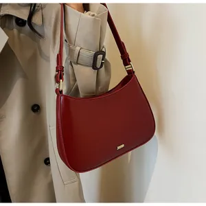 Close-up of deep red half-moon shoulder bag with gold hardware and leather shoulder strap