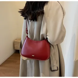 Detail of burgundy half-moon underarm bag featuring a metallic JAGOR logo and sleek leather texture