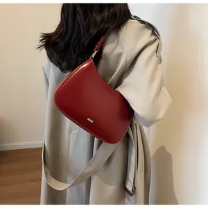 Model wearing a dark red underarm bag with gold logo over a khaki trench coat