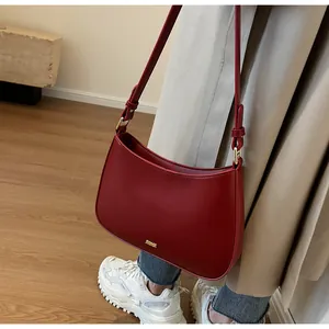 Deep red leather crescent underarm bag styled with a neutral trench coat and casual wear