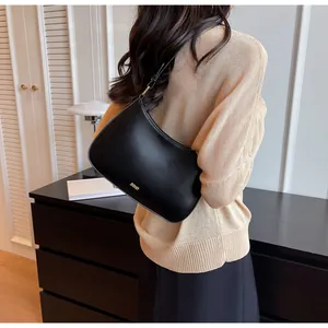 Detail of minimalist black crescent underarm bag with gold logo on smooth leather texture