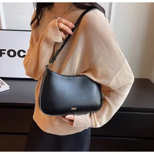 Close-up of minimalist black leather crescent bag featuring a gold metal logo detail